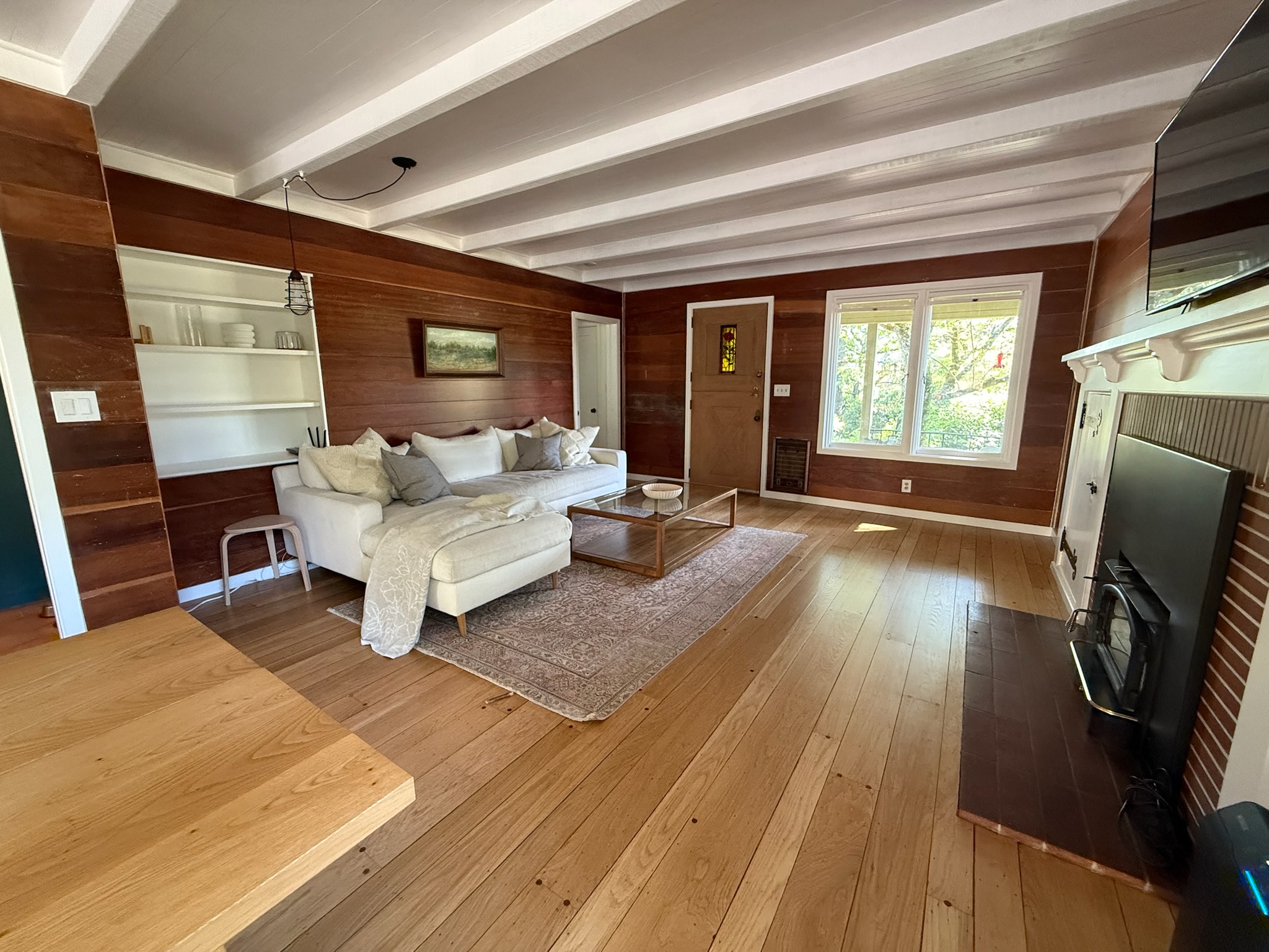 The living room exudes relaxed sophistication with warm wood-paneled walls, a plush sectional sofa, and curated art. Natural light pours through oversized windows, connecting indoors with out.