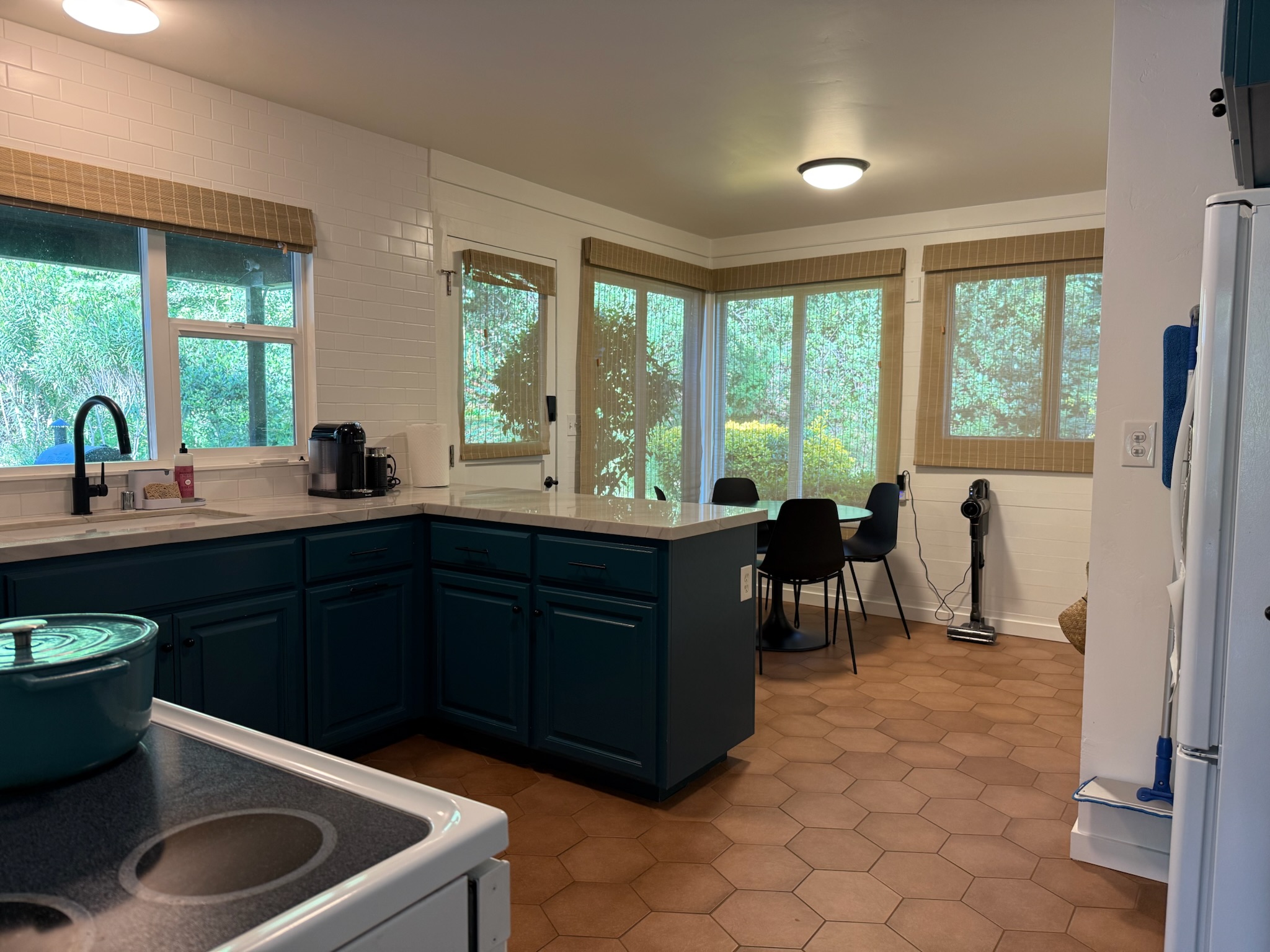 The cheerful, light-filled kitchen features teal cabinetry, marble-style countertops, and a breakfast nook overlooking the gardens, perfect for easy mornings at home.